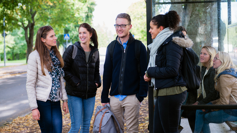 Sju studenter väntar på bussen vid en busshållsplats. Foto Eva Dalin